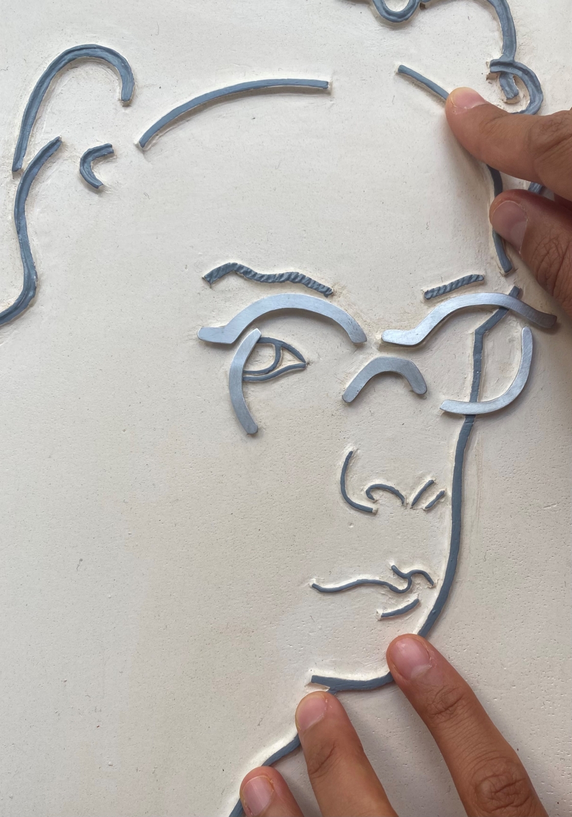 Mãos a tatearem desenho de rosto em relevo.